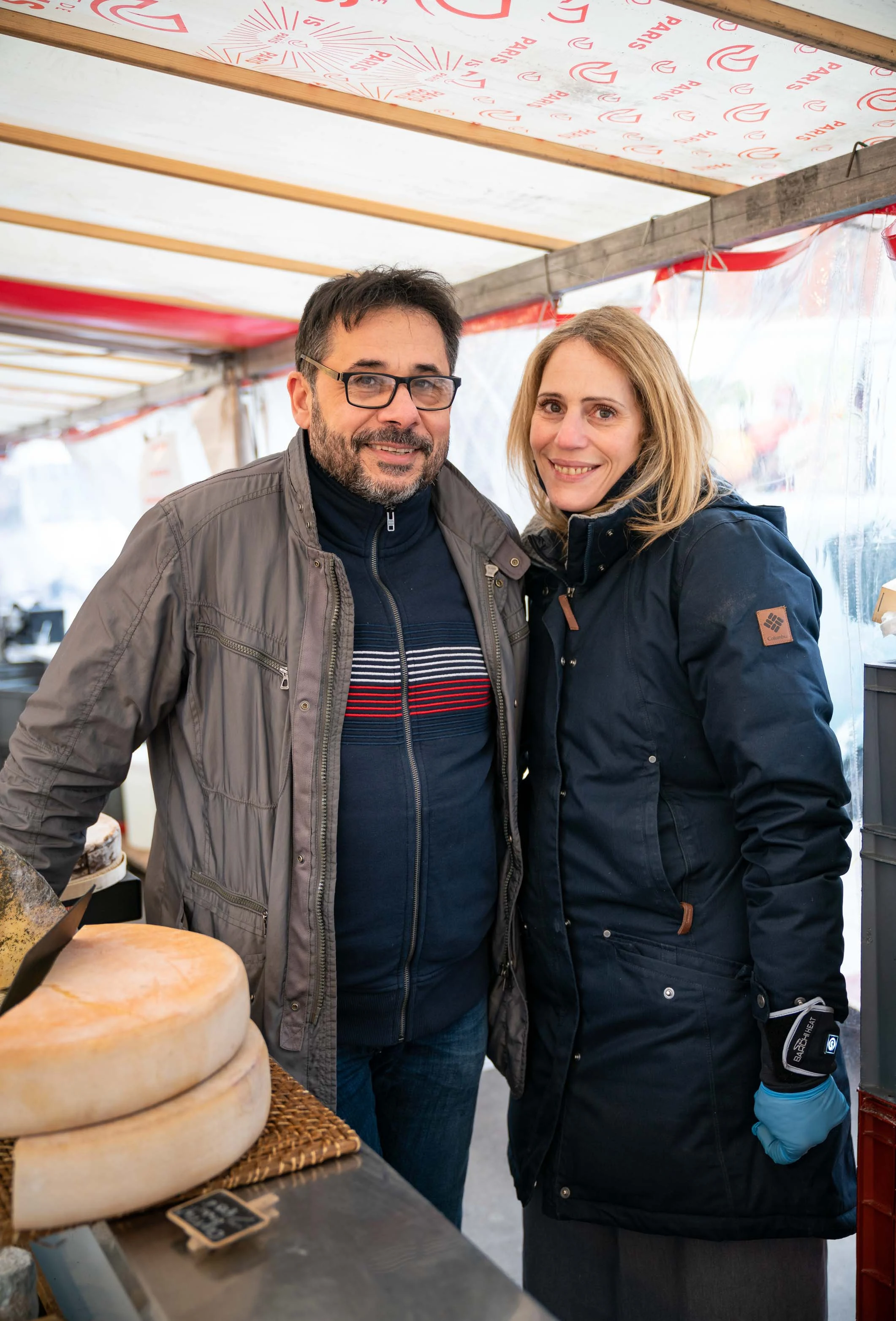 Deux personnes posent derrière une meule de fromage, sur le stand d'un fromager