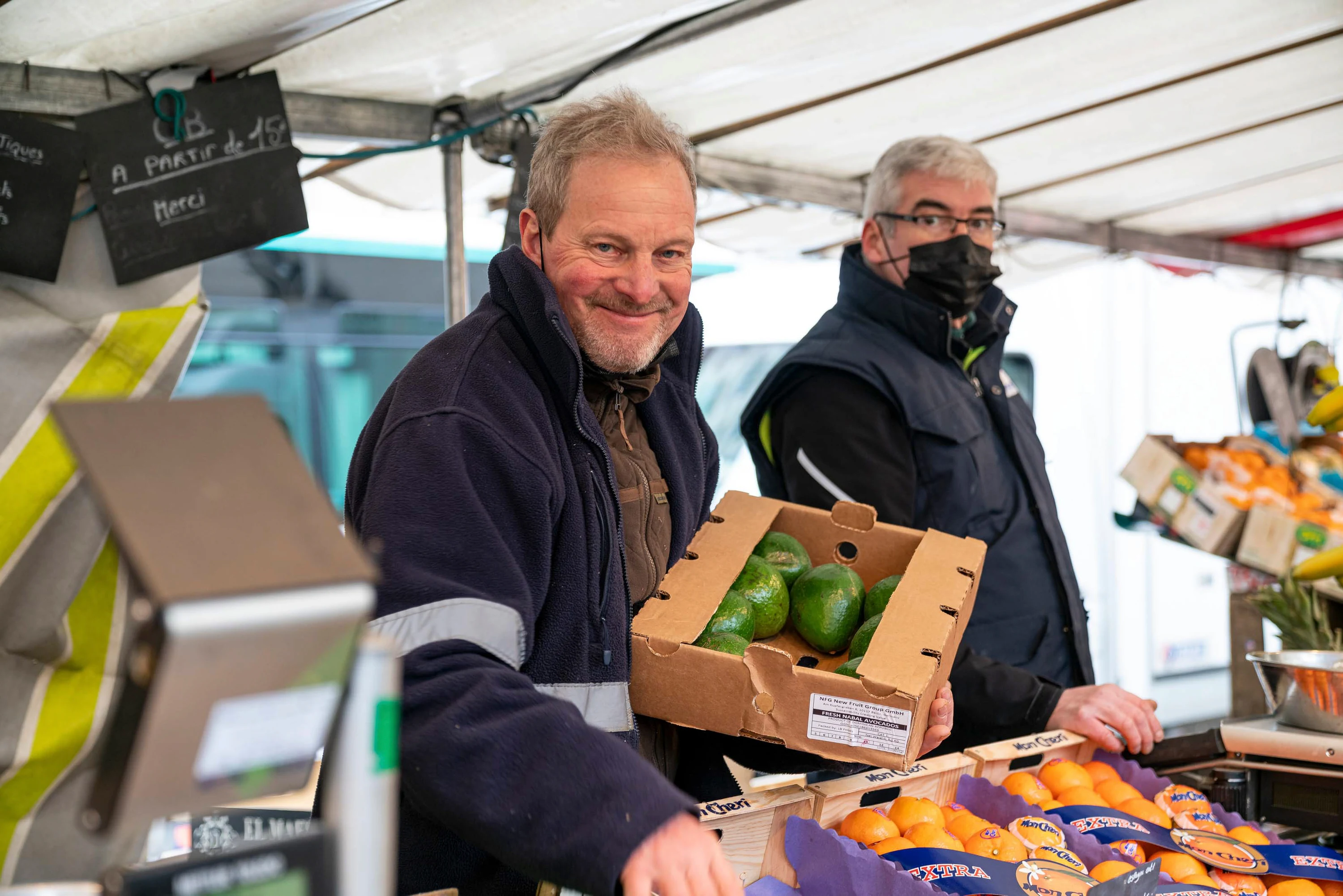 Un maraîcher présente un carton d'avocats sur son stand