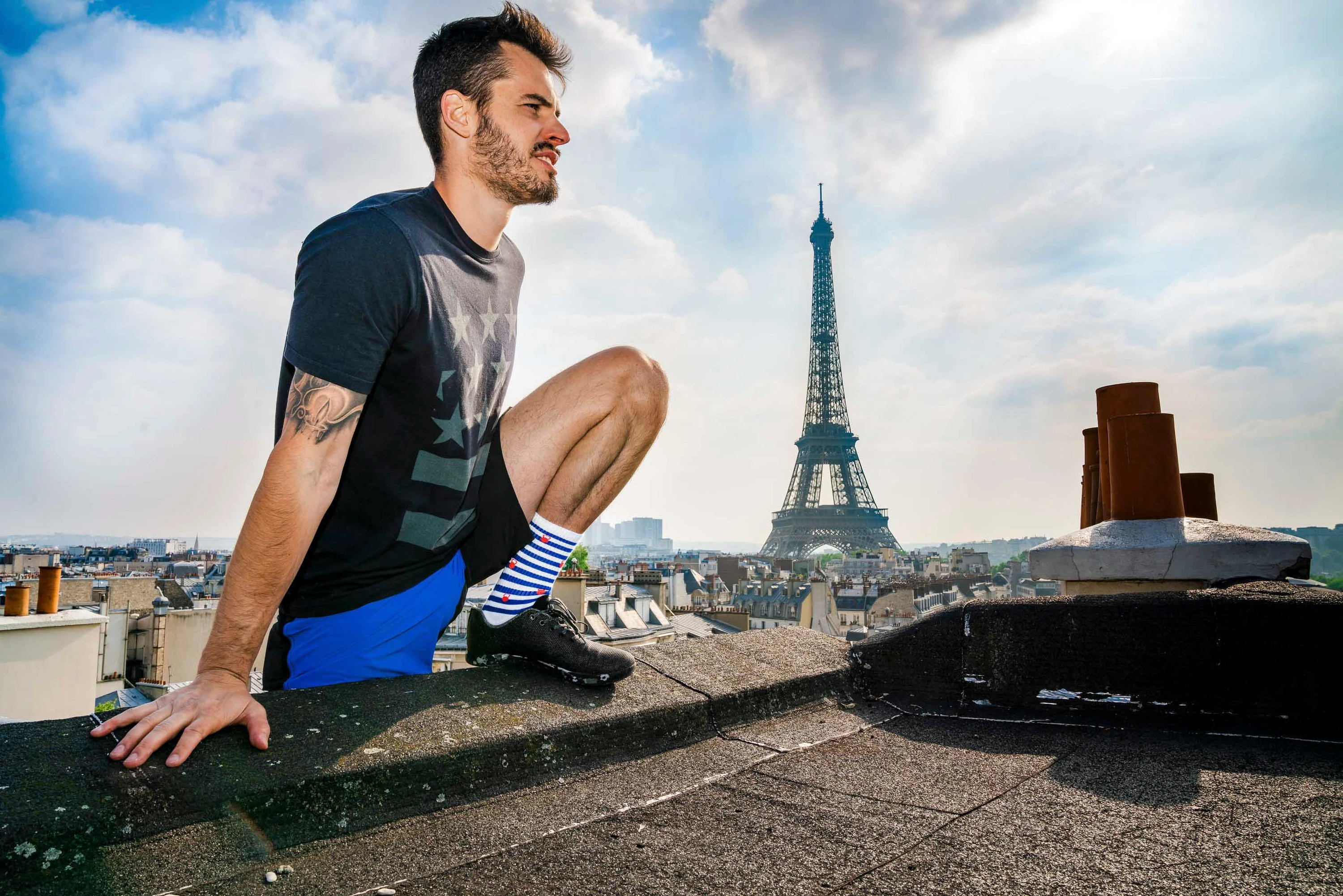 Un athlète accroupi sur un toit, la tour Eiffel dans l'axe