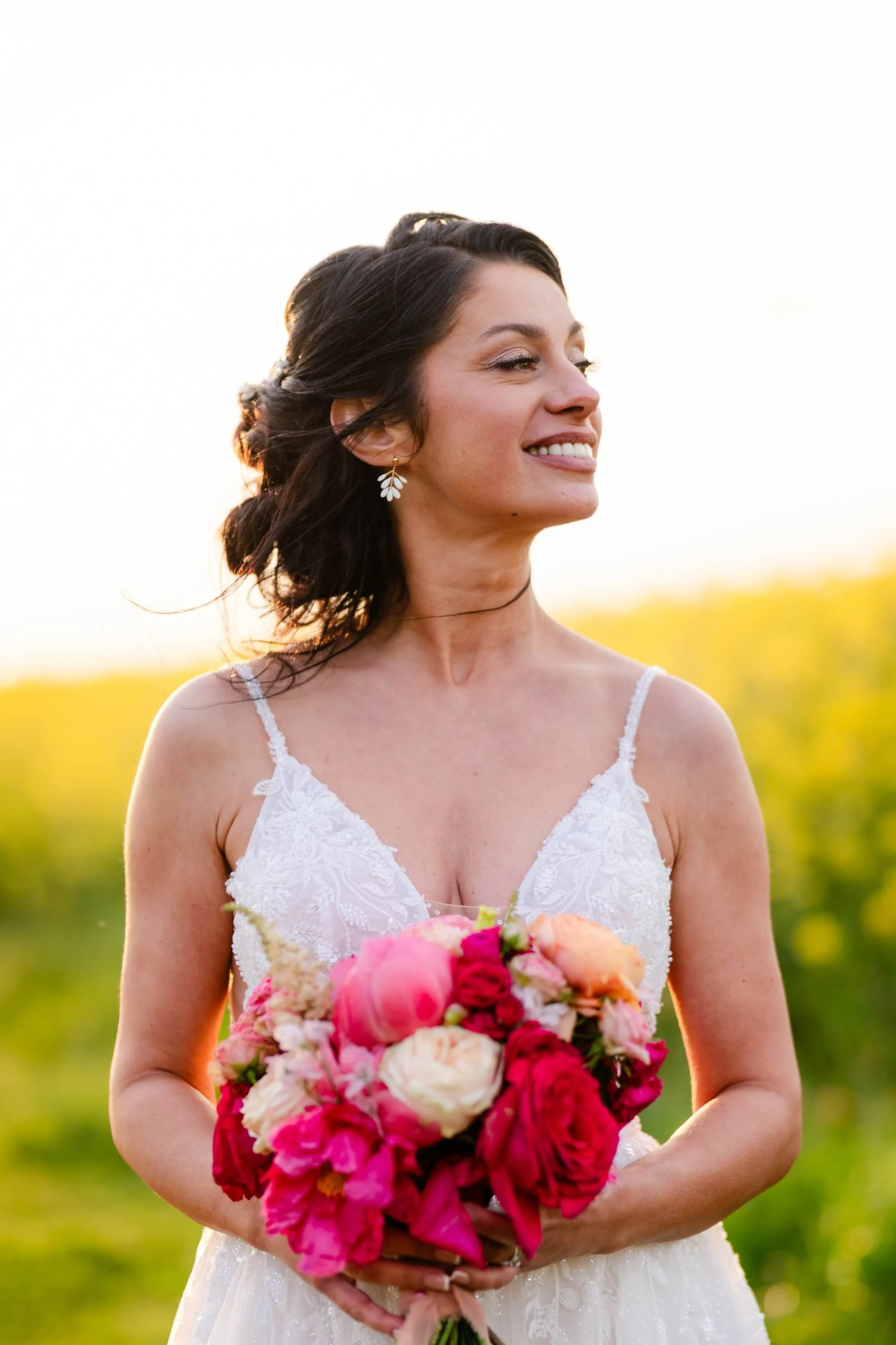 Portrait d'une mariée tenant un bouquet rose et corail devant un champ de colza