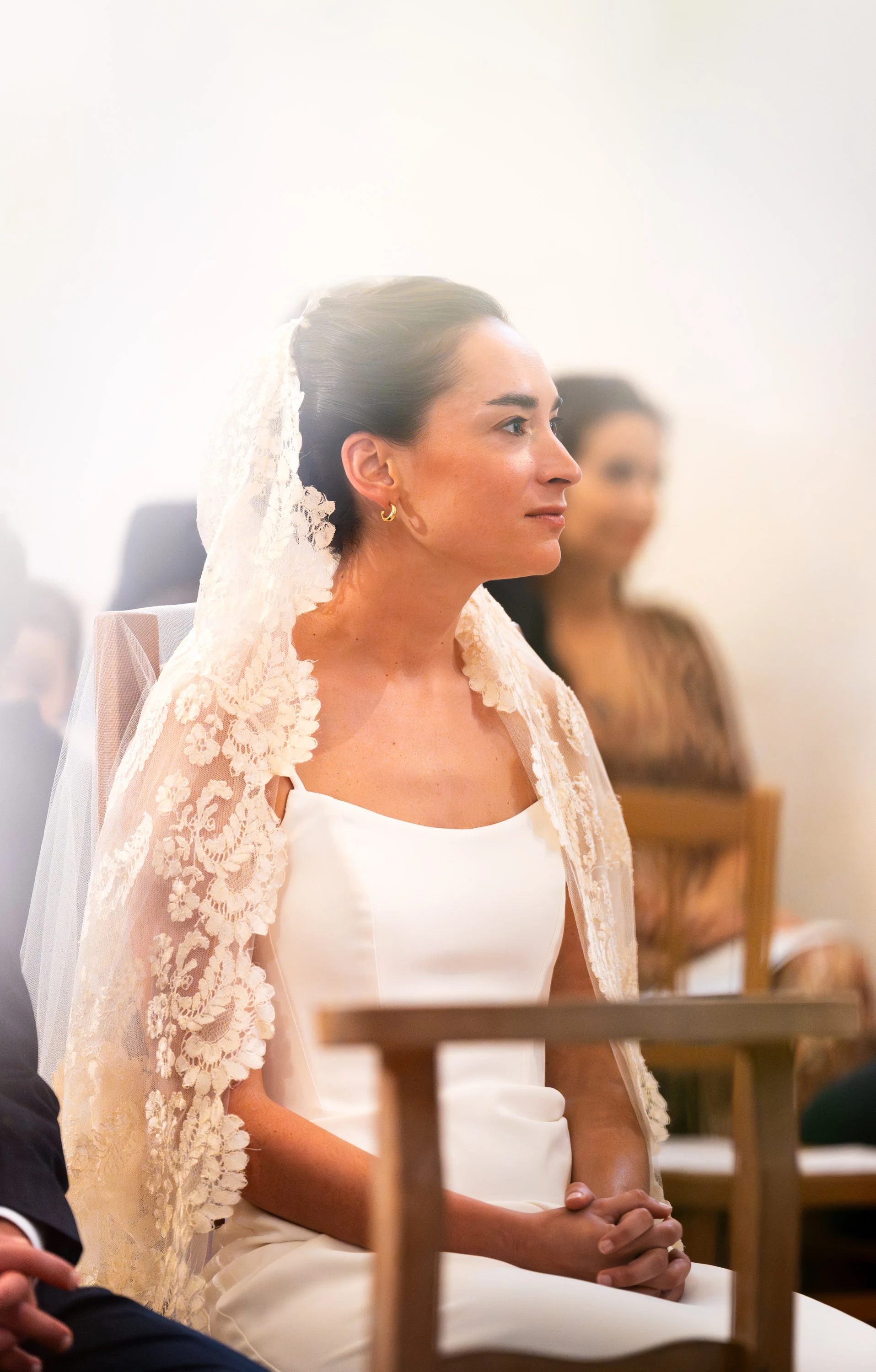 Une mariée assise pendant la cérémonie, mantille de dentelle sur les cheveux