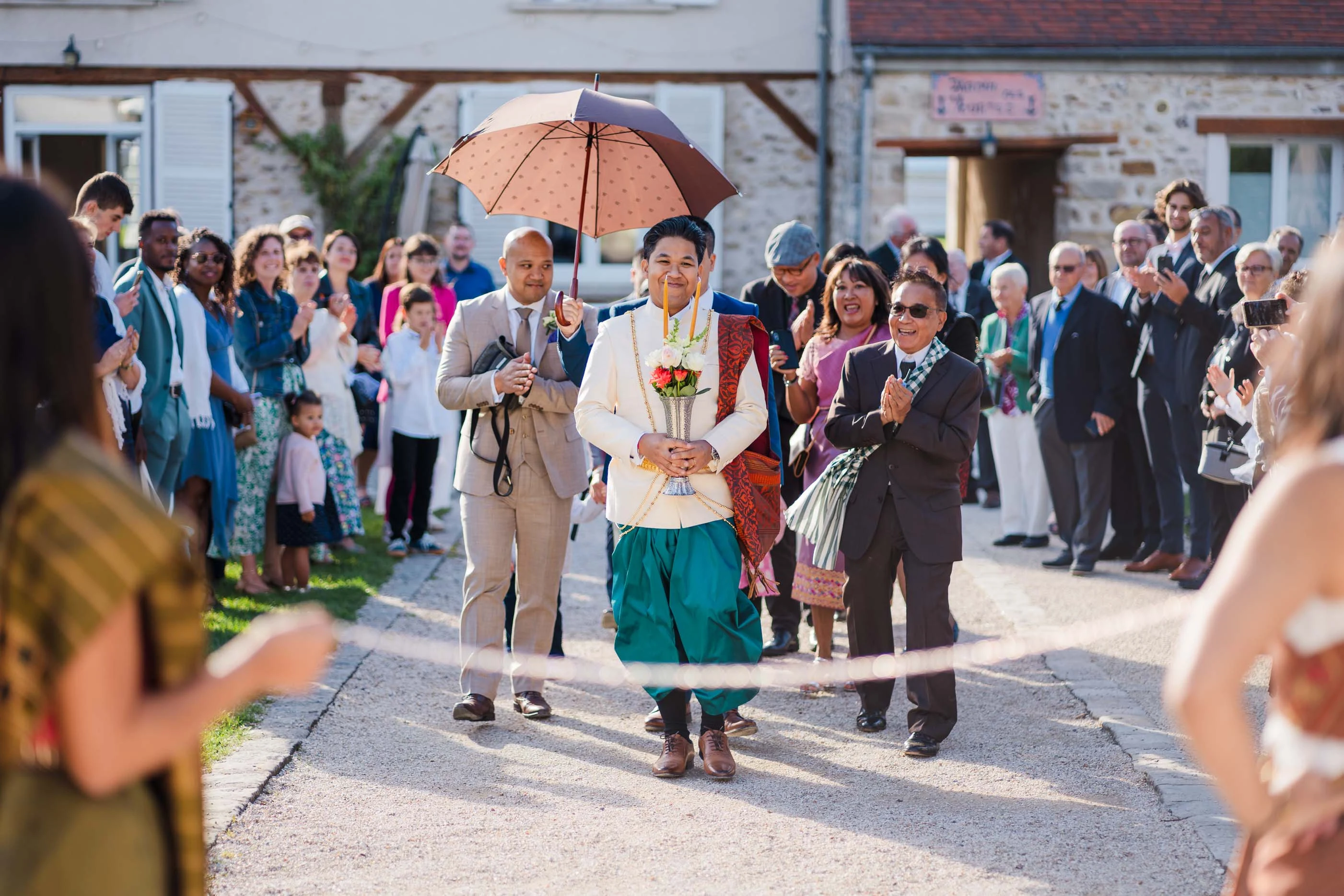 Cortège de mariage sous une ombrelle, entre deux haies d'invités