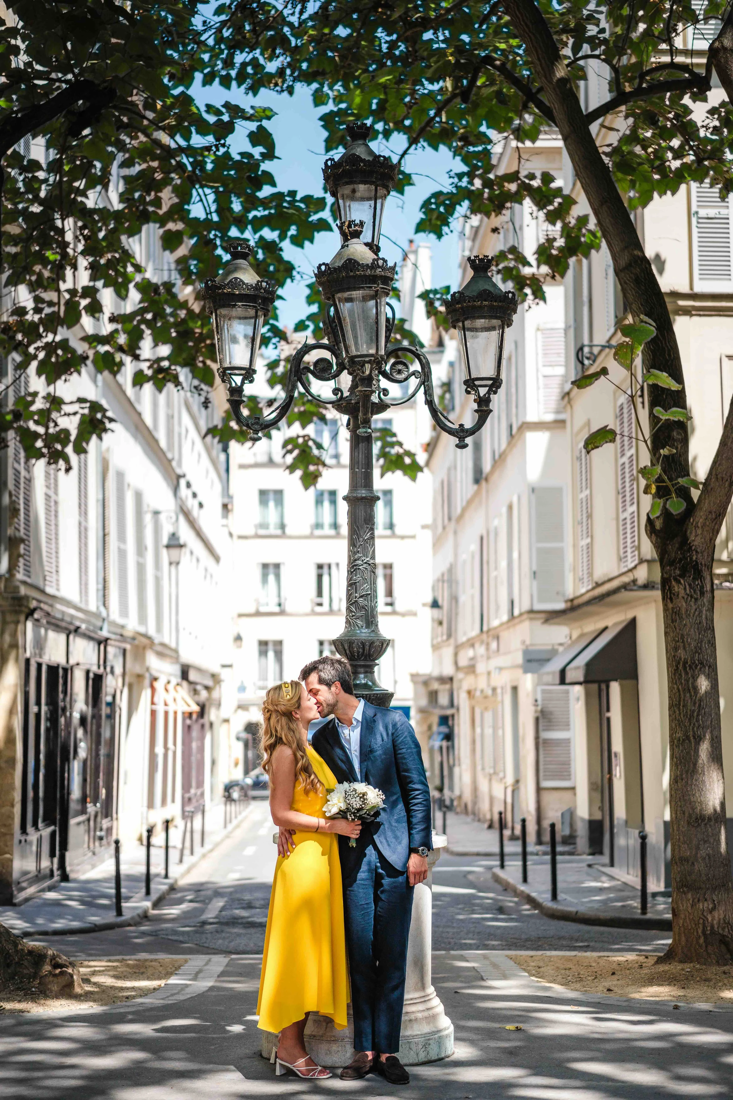 Les mariés s'embrassent au milieu d'une rue parisienne bordée d'arbres