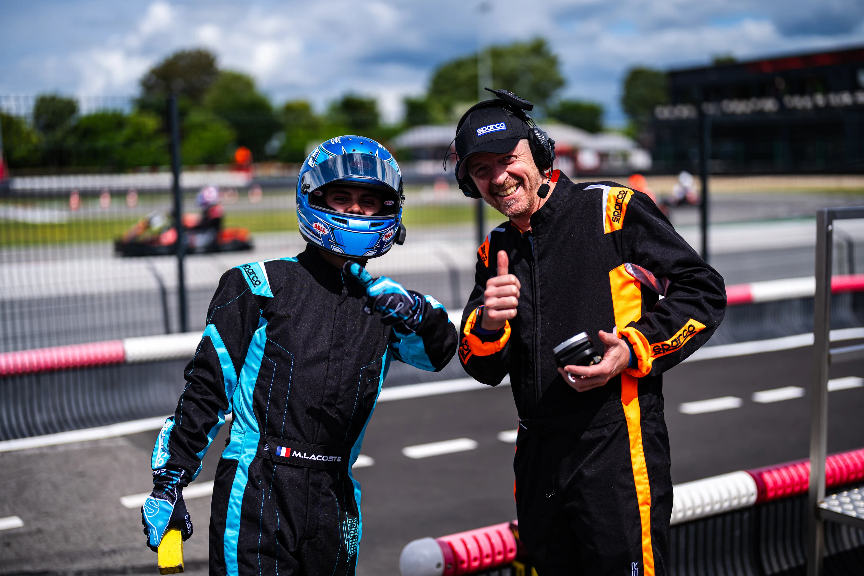 Un pilote et son mécanicien échangent au bord de la piste, casque relevé