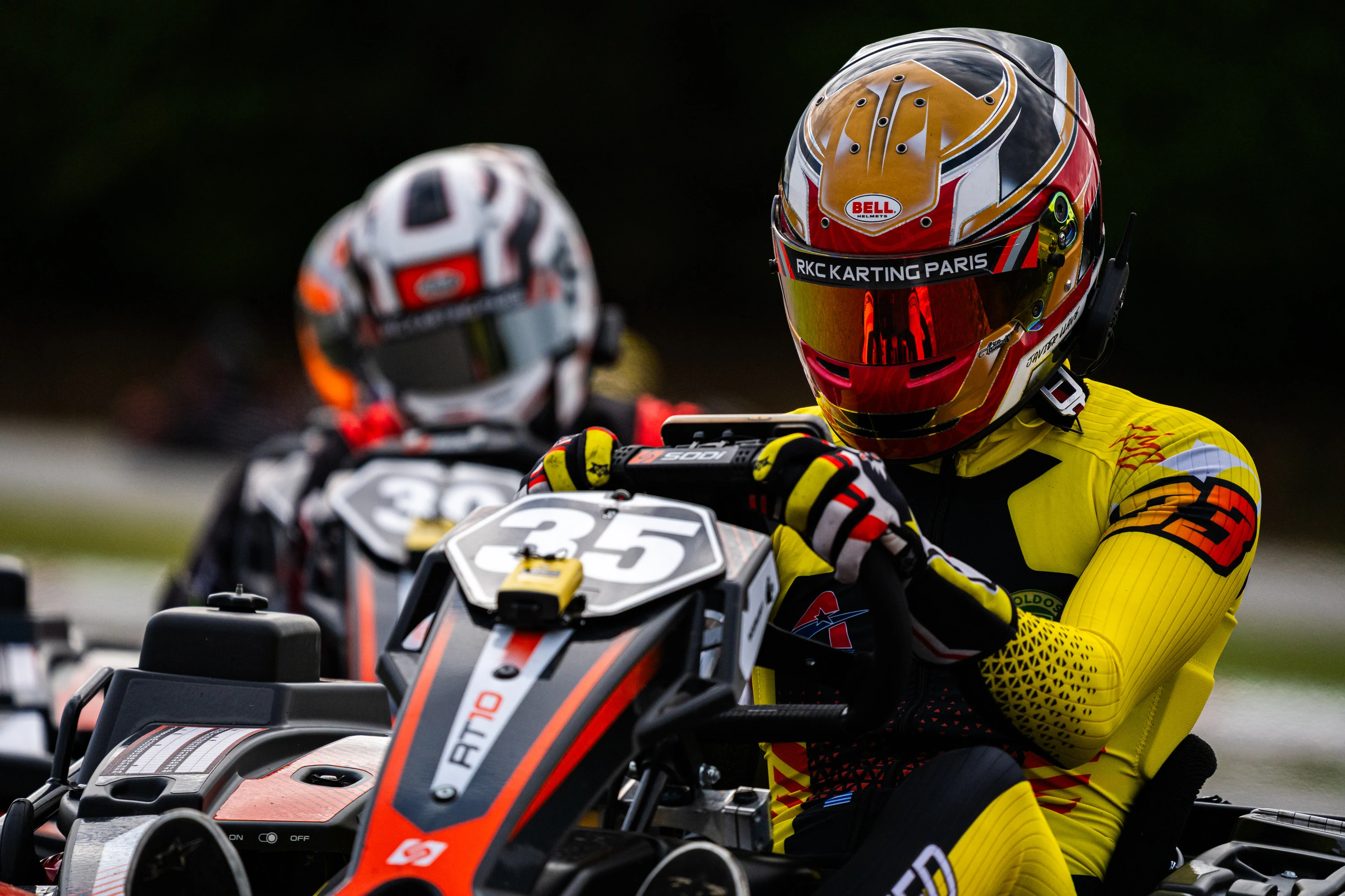 Deux pilotes de karting roue dans roue, visages concentrés derrière les visières