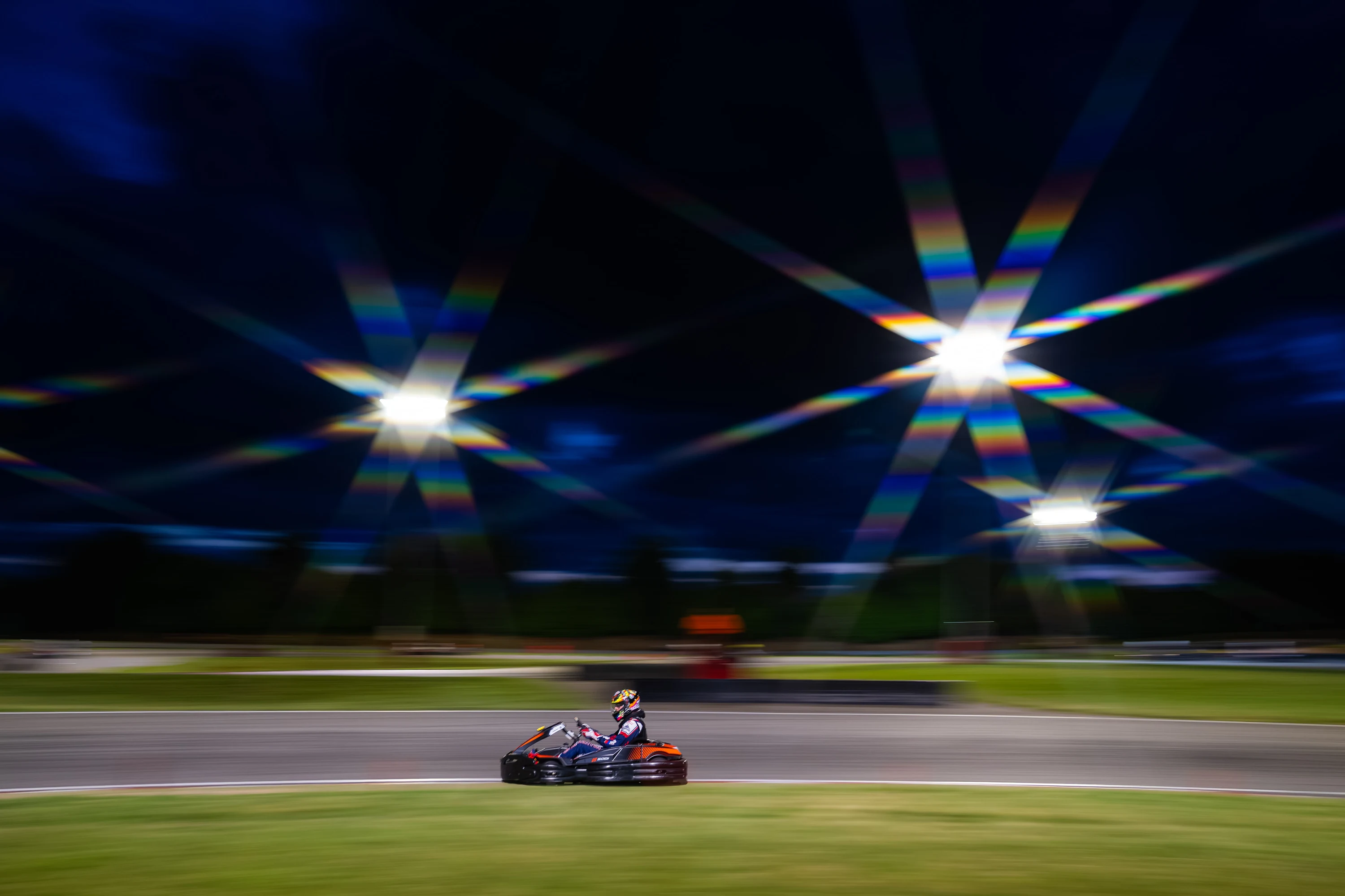 Un kart file sous les projecteurs de la nuit, étoiles de lumière au-dessus de la piste