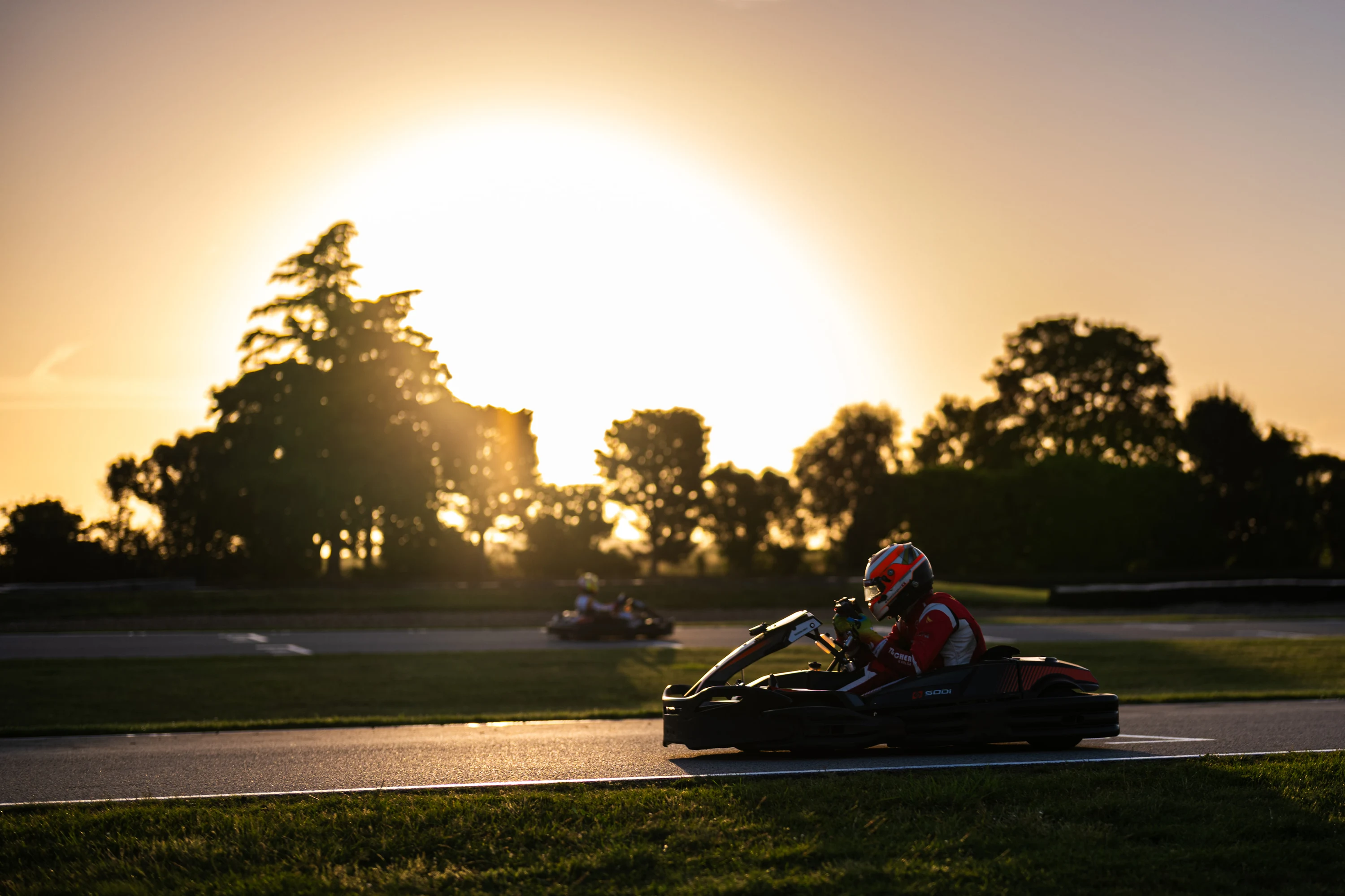 Un kart passe devant le soleil couchant, silhouettes d'arbres en fond
