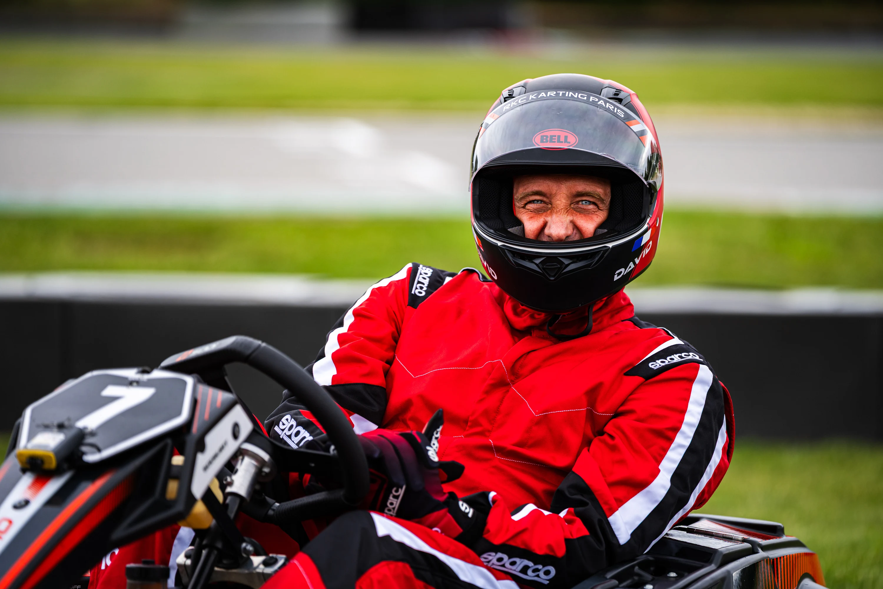Portrait d'un pilote souriant dans son kart, casque ouvert