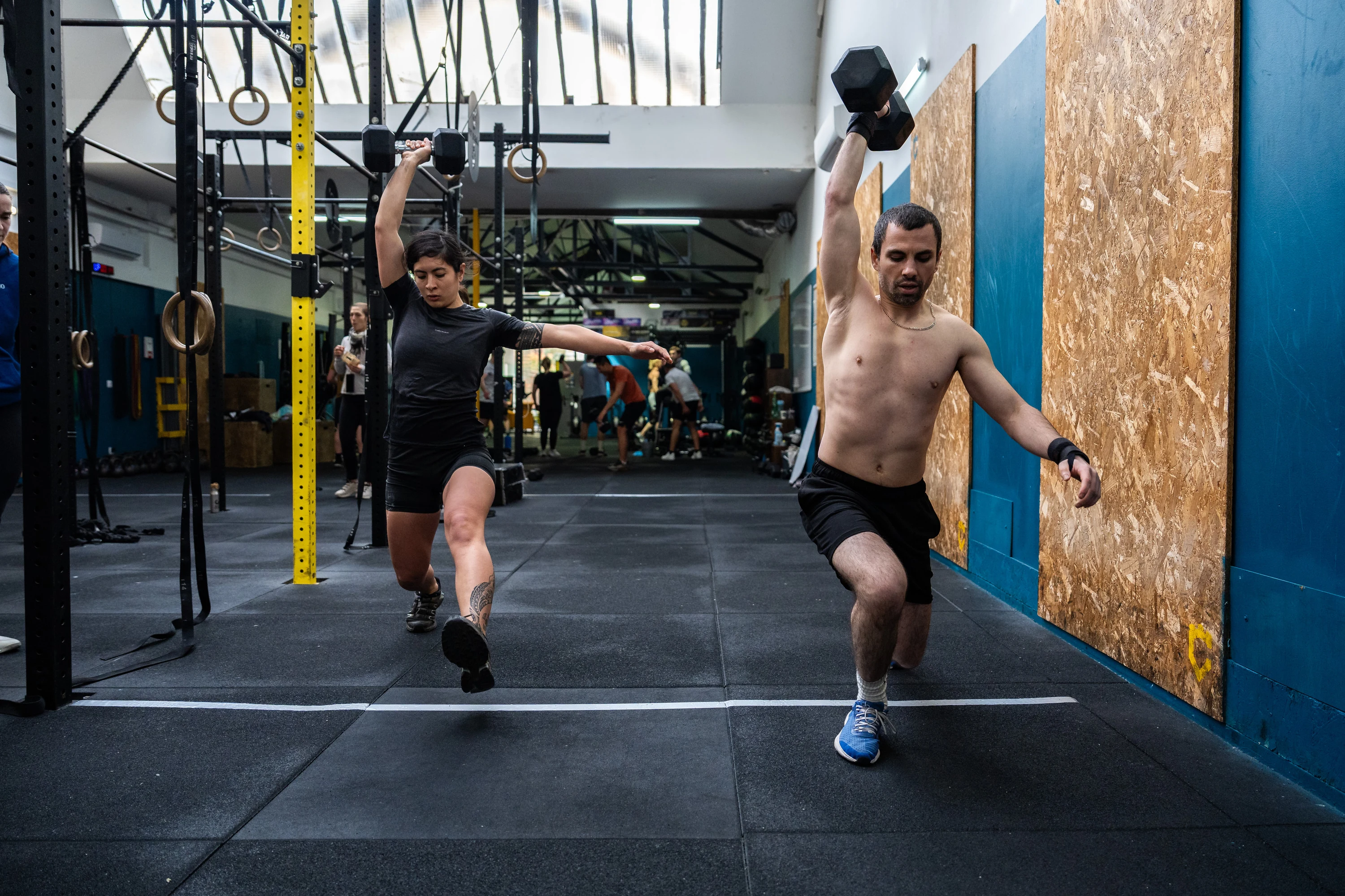 Deux athlètes sprintent côte à côte dans la salle, haltères en main