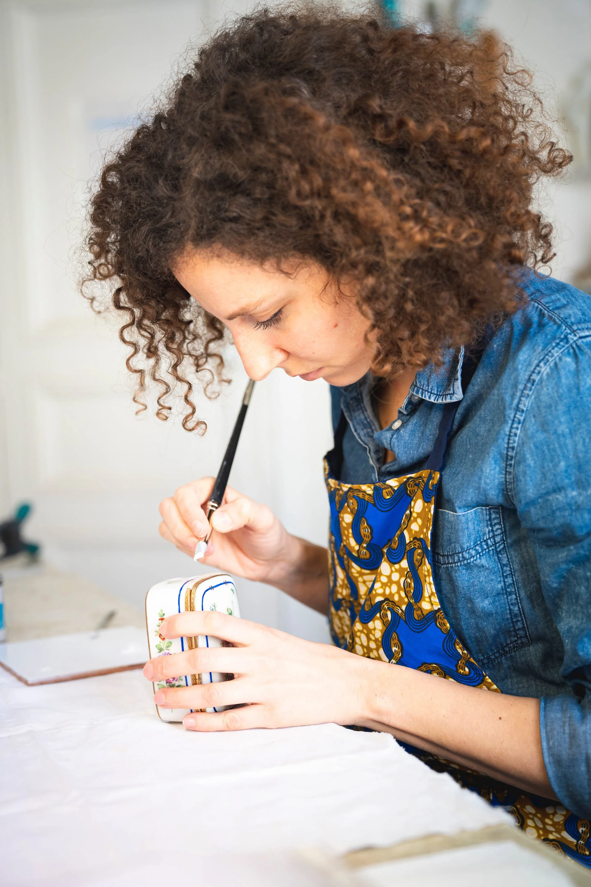 Une artisane peint un décor doré sur une pièce de porcelaine