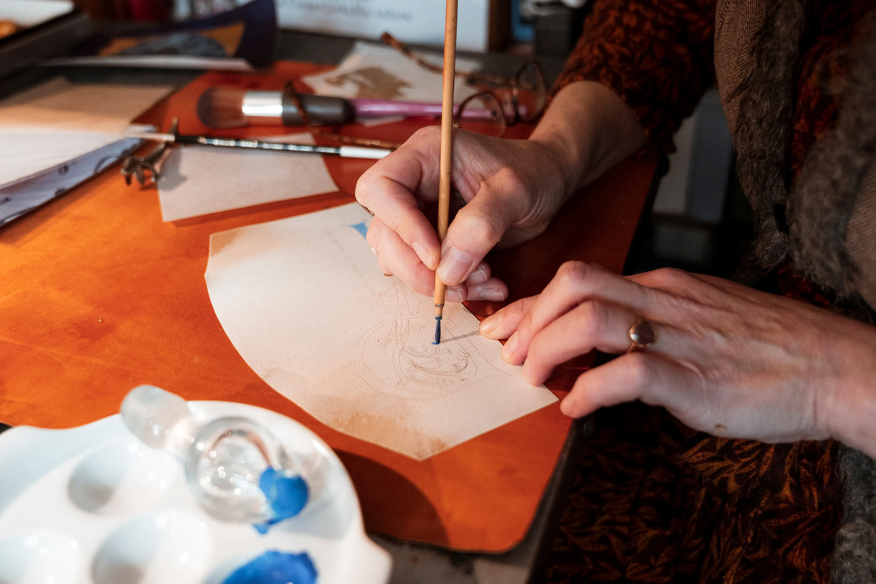 Une artisane peint un motif au pinceau sur un cuir, sa palette à côté