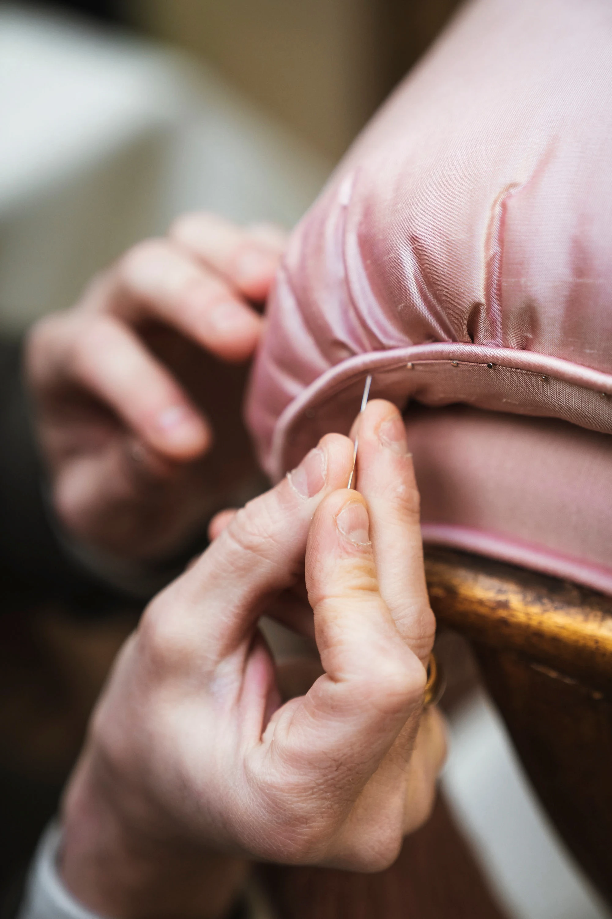Des mains cousent un tissu rose sur un cadre doré