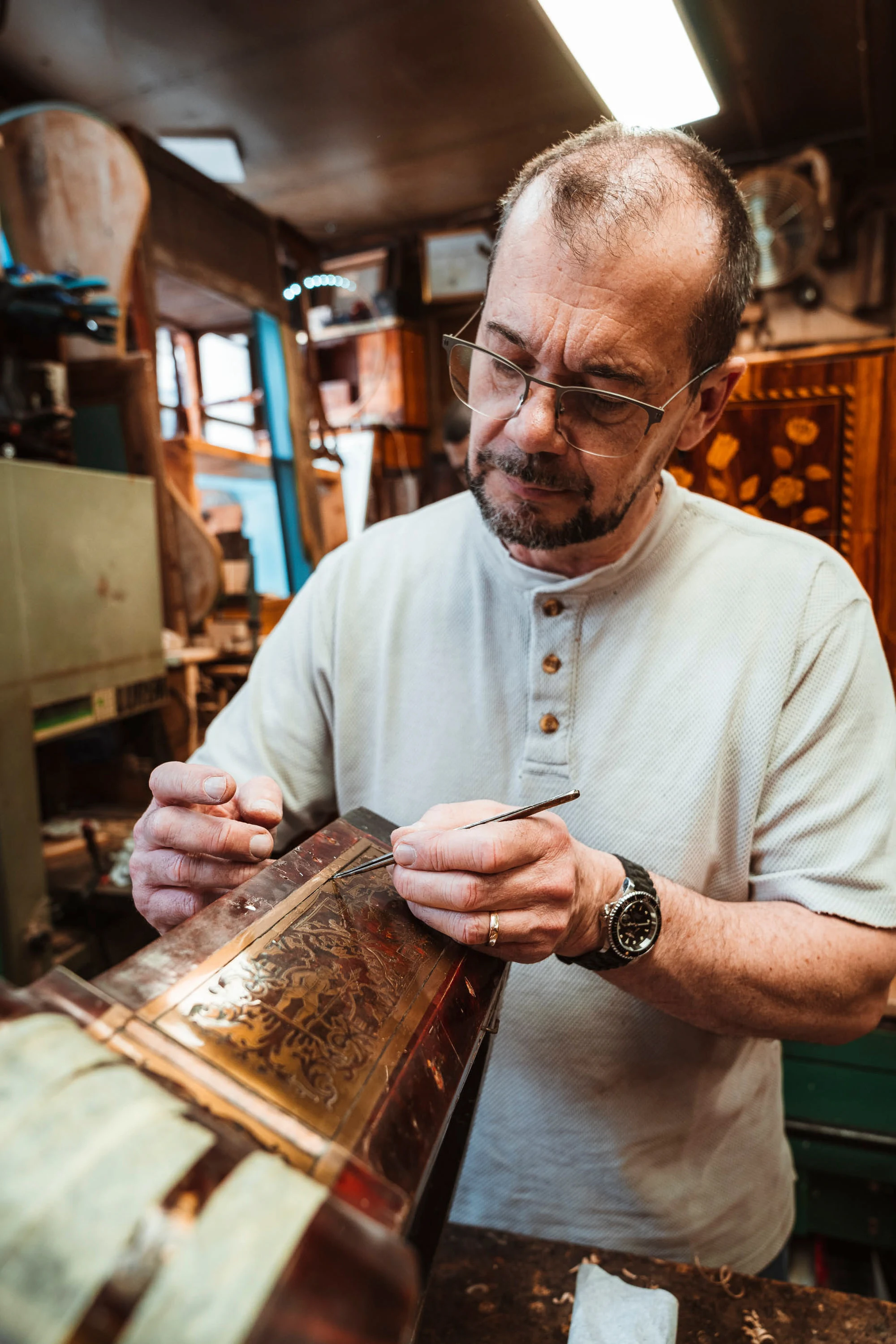 Un artisan retouche un panneau de marqueterie dans son atelier