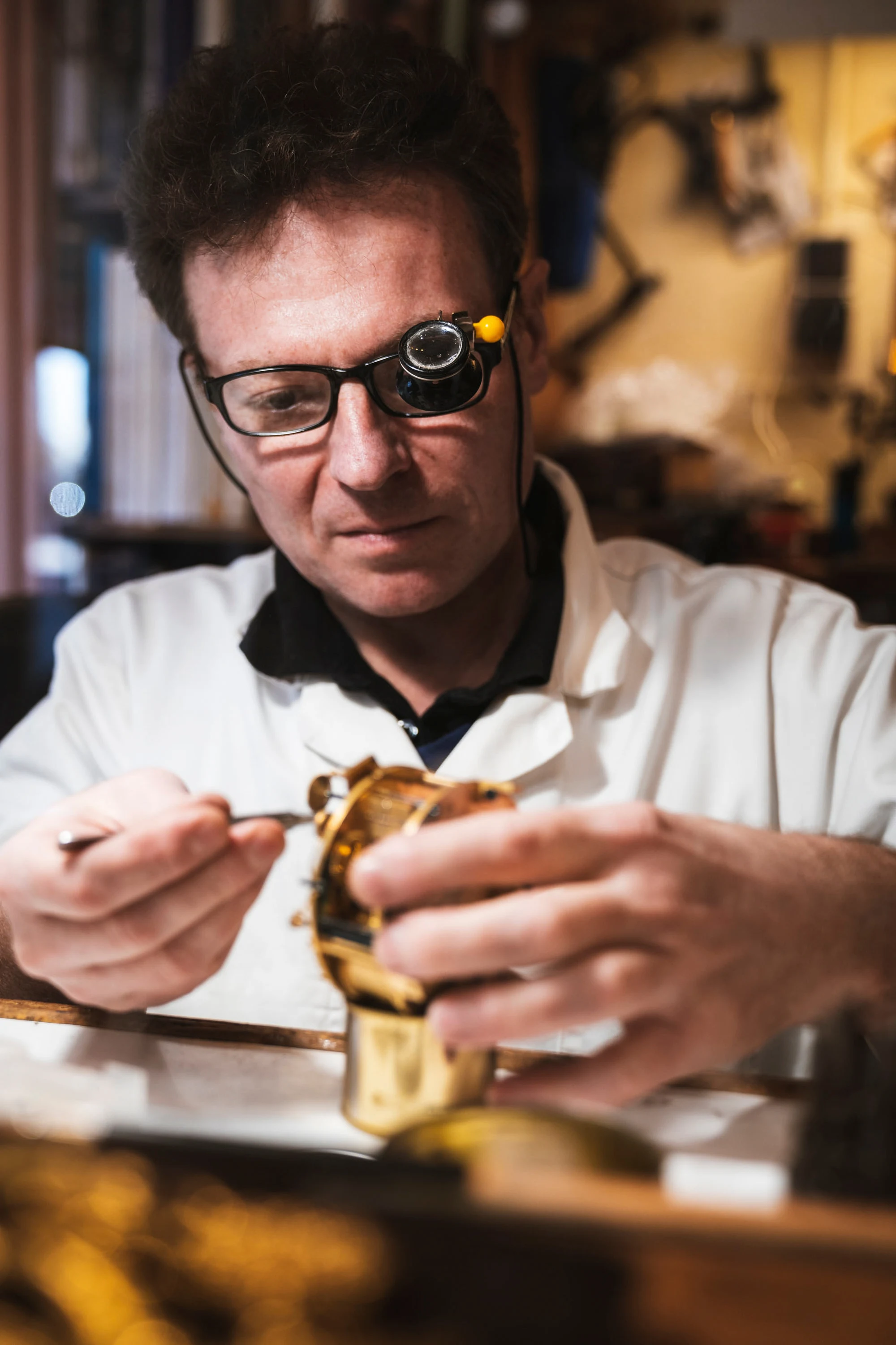 Un artisan travaille une pièce de bronze, loupe frontale sur les yeux