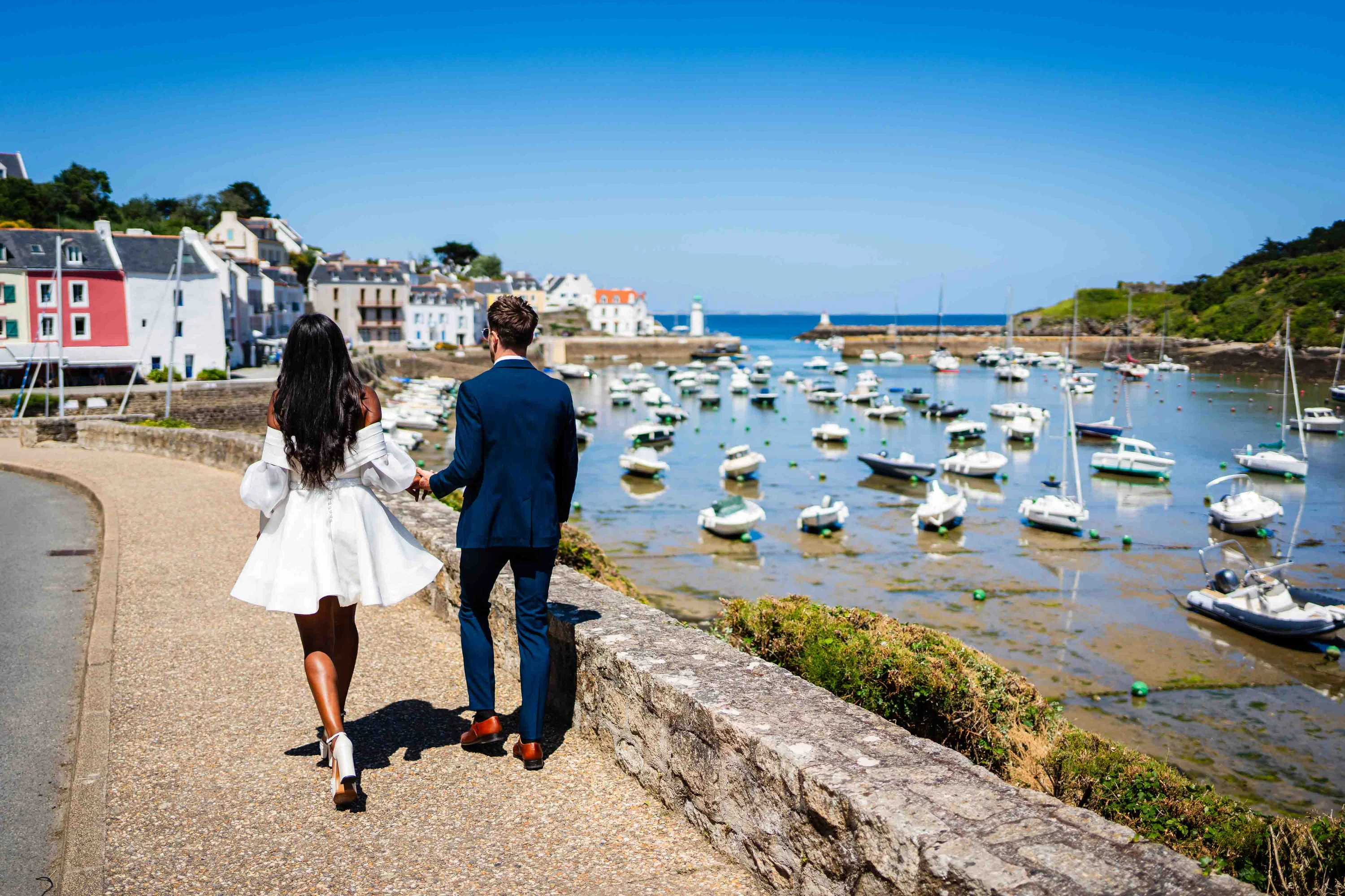 Amandine et Benjamin marchent le long du port de Belle-Île-en-Mer, les bateaux au mouillage derrière eux