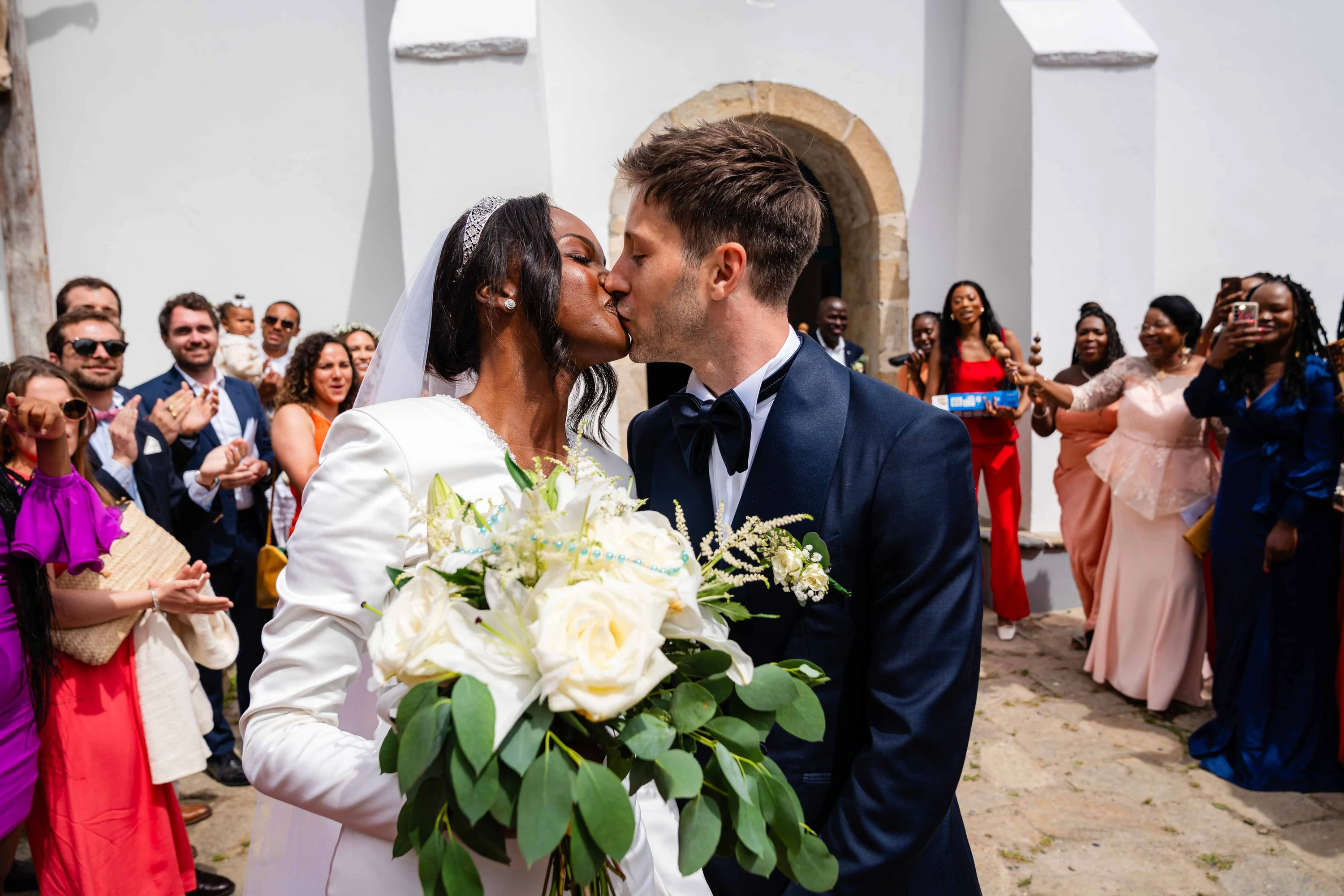 Le baiser des mariés sur le parvis de l'église, entourés des invités