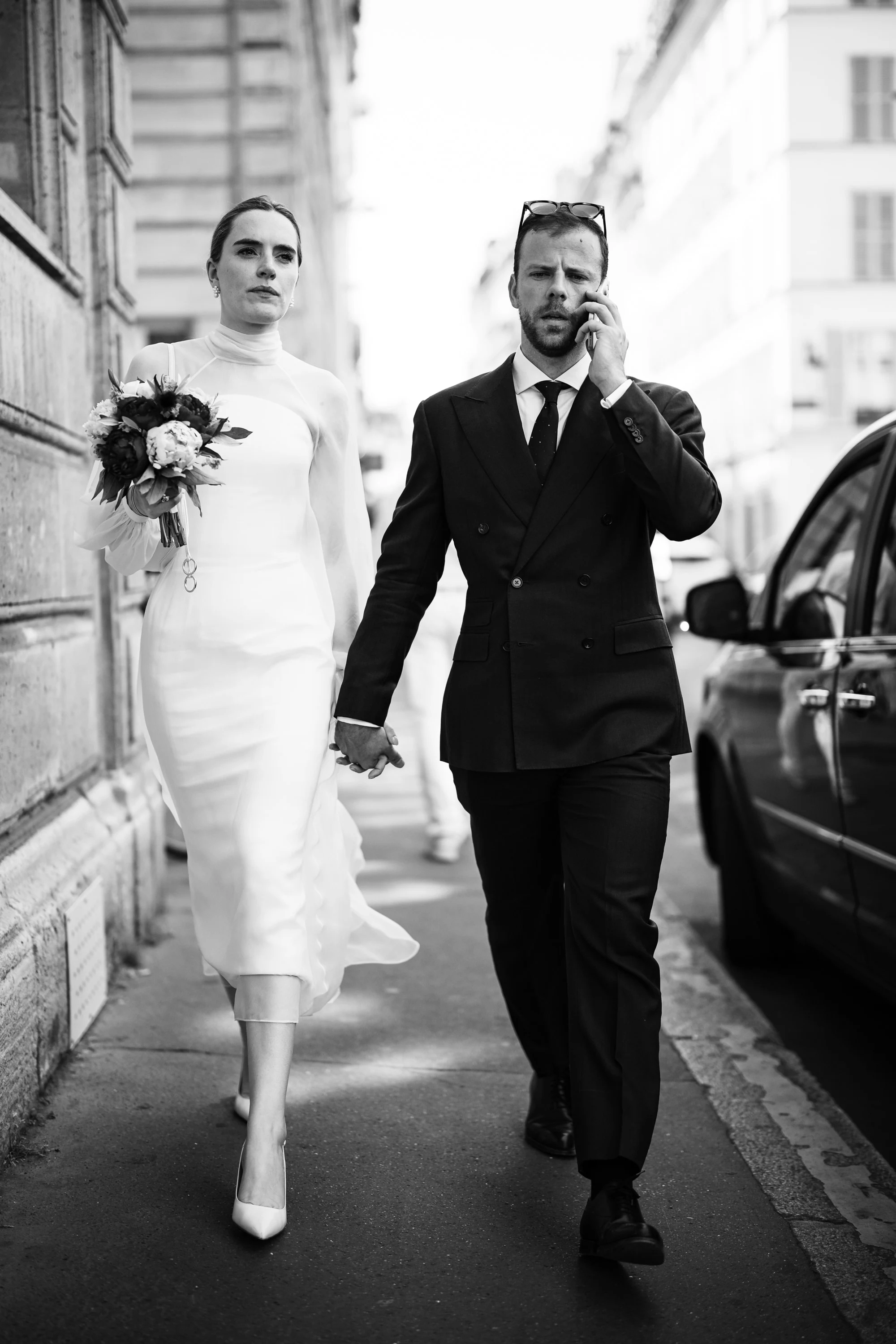 Les mariés remontent la rue, Thomas au téléphone, en noir et blanc